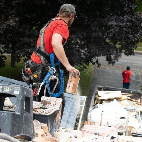 A professional man in a red shirt and vest is stacking bricks beside a dumpster truck.